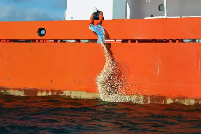 En person häller ut popcorn ur en blå påse ner i vatten